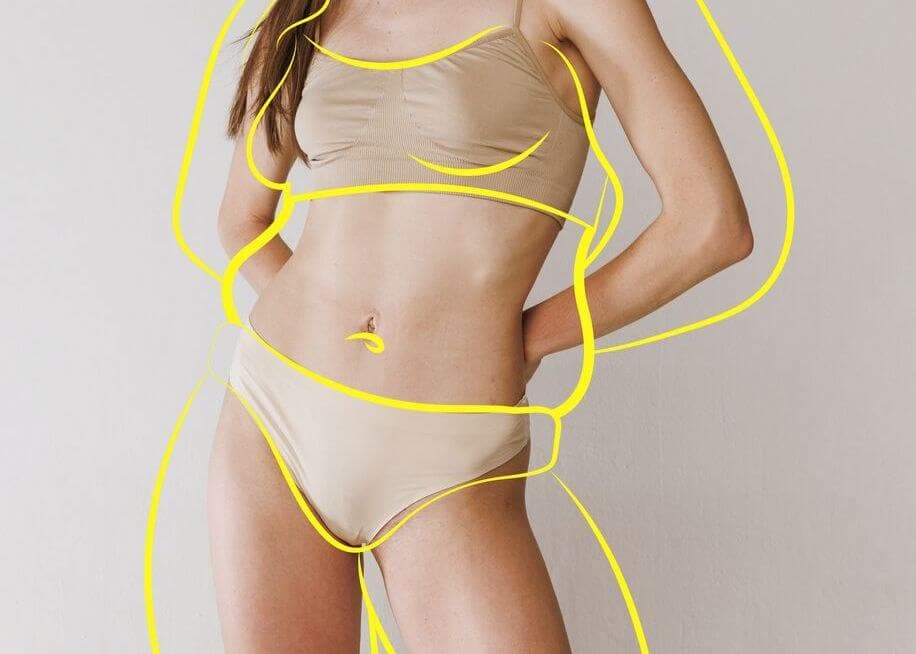 Mulher com roupa íntima bege posa com contornos amarelos desenhados sobre o corpo, representando as áreas tratadas durante uma lipoaspiração para remodelar o contorno corporal.