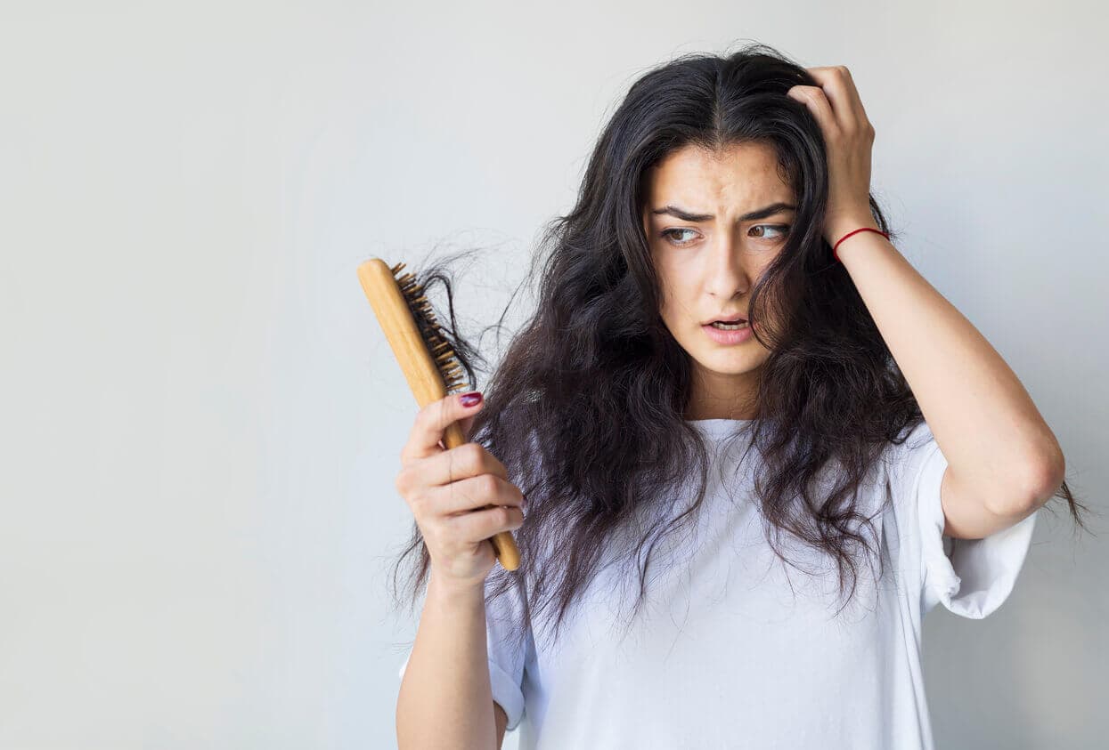 Mulher com expressão preocupada segurando uma escova cheia de fios de cabelo, observando sinais de queda de cabelo