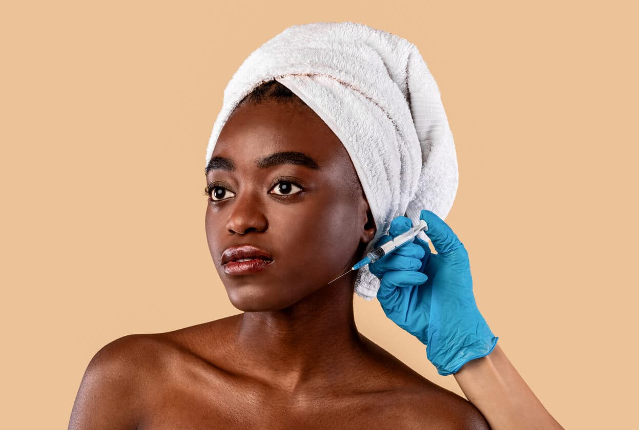 Mulher com toalha enrolada no cabelo, recebendo tratamento estético no rosto