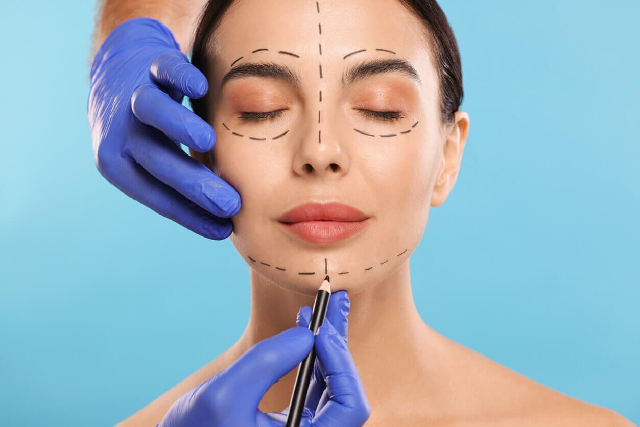 Médico desenhando marcas no rosto de uma mulher para operação de cirurgia estética.