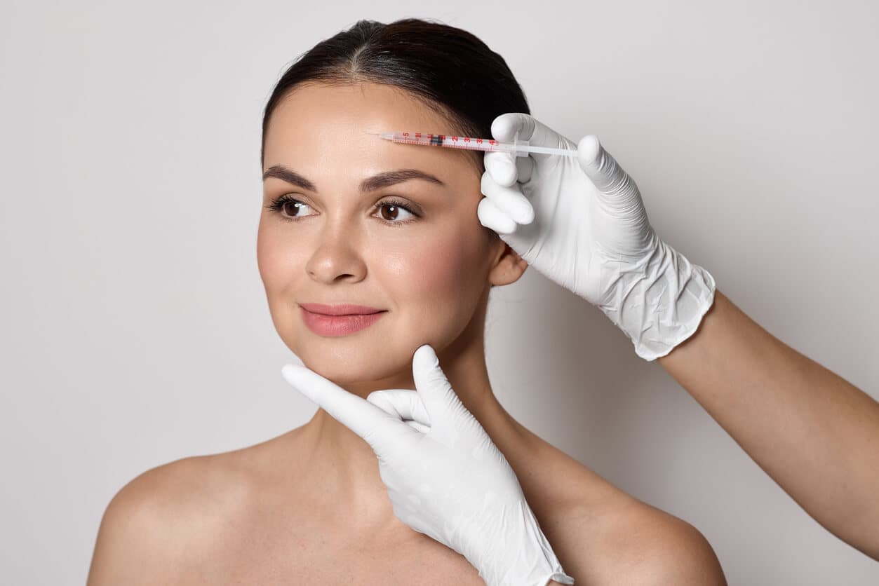 Mulher recebendo aplicação de botox no rosto, com expressão serena, enquanto profissional usa luvas e seringa para o procedimento estético na região da testa.