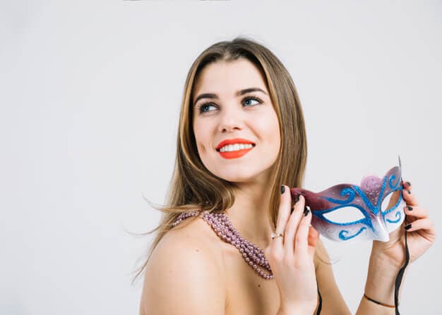 mulher sorrindo de batom vermelho segurando uma máscara de carnaval