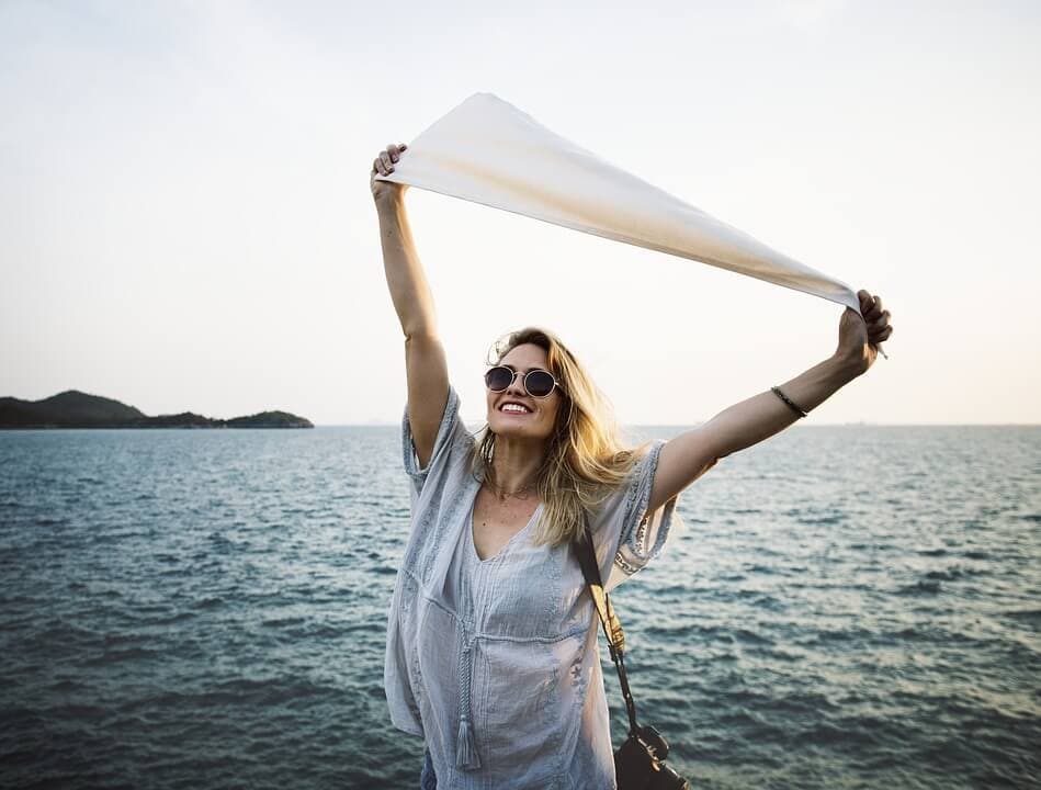 mulher feliz na praia segurando um pano e sorrindo