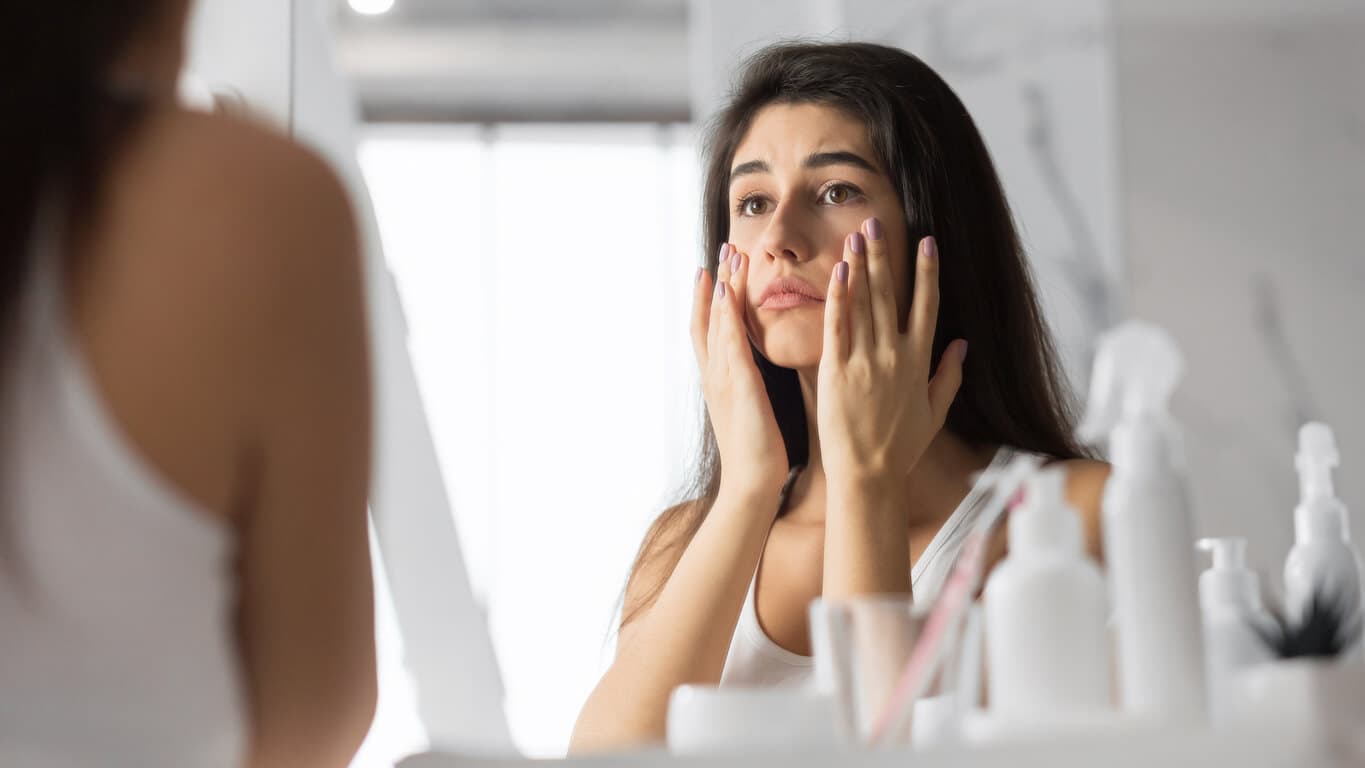 Mulher que sofre com olheiras olhando no espelho
