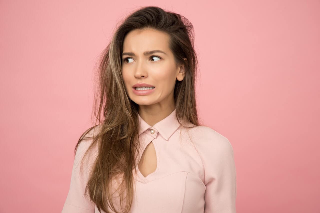 Mulher em fundo rosa com a expressão preocupada