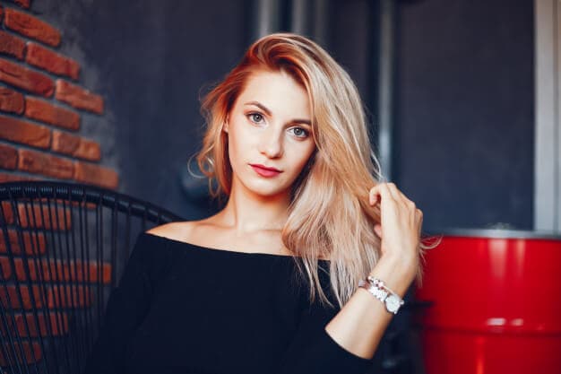 mulher loira sentada com a mão no cabelo olhando para a câmera