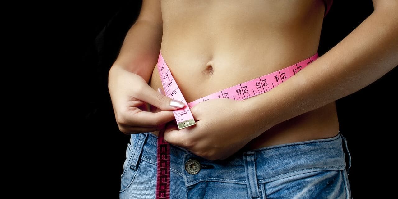 Barriga chapada de mulher tirando as medidas nas fitas métricas