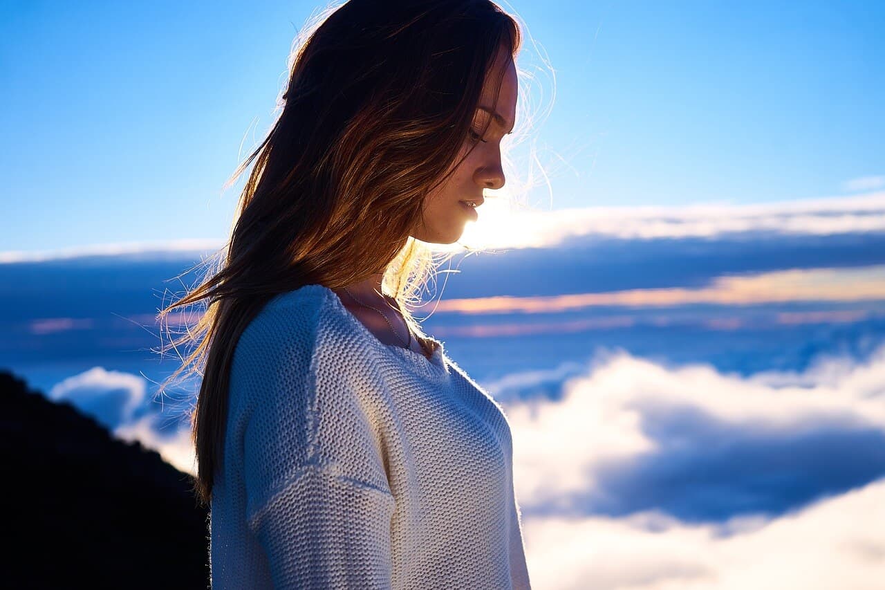 Mulher de cabeça baixa e nuvens ao fundo