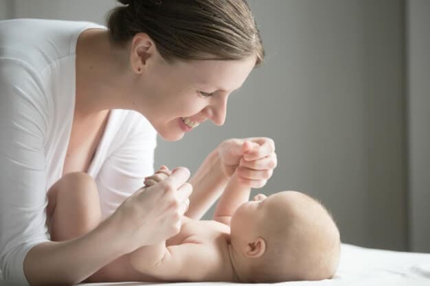mãe sorrindo brincando com o bebê deitando na cama