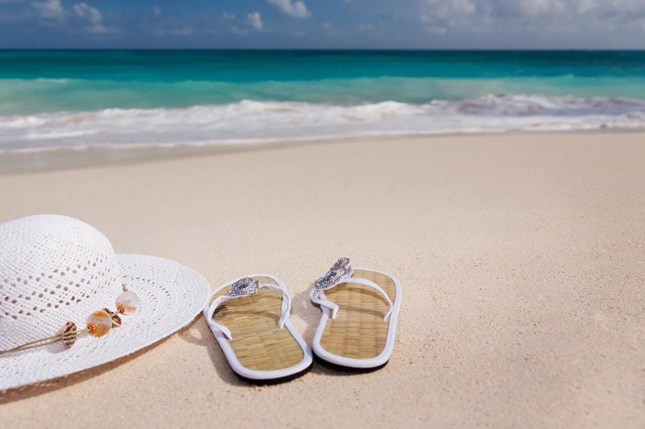 Praia com chapéu e chinelo na areia