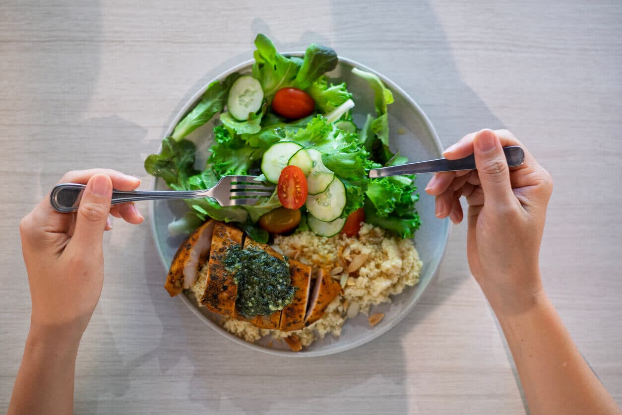Prato saudável com frango grelhado, salada de folhas, tomate, pepino e grãos, visto de cima.