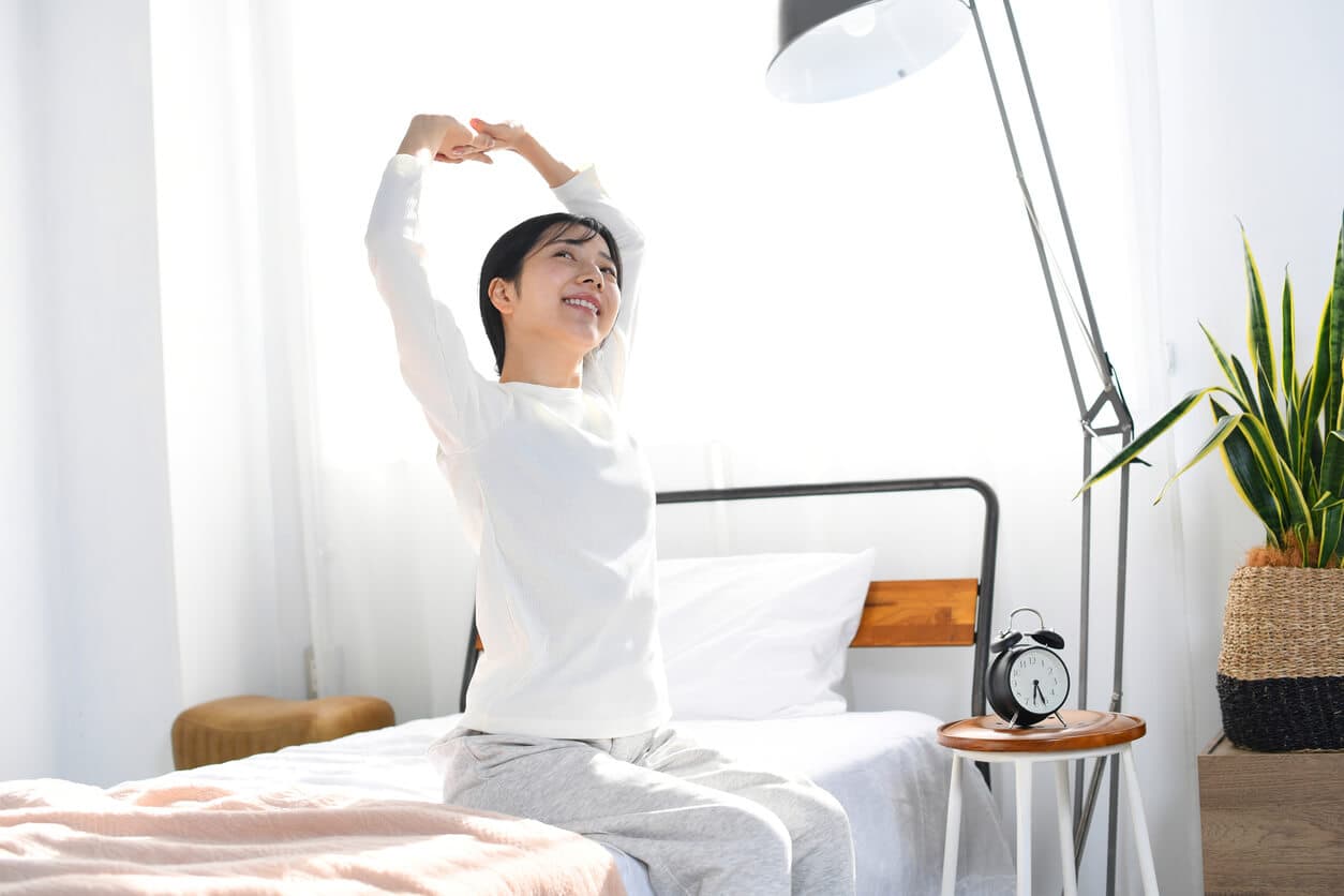 Mulher fazendo alongamento matinal ao acordar para aliviar a tensão e prevenir dores