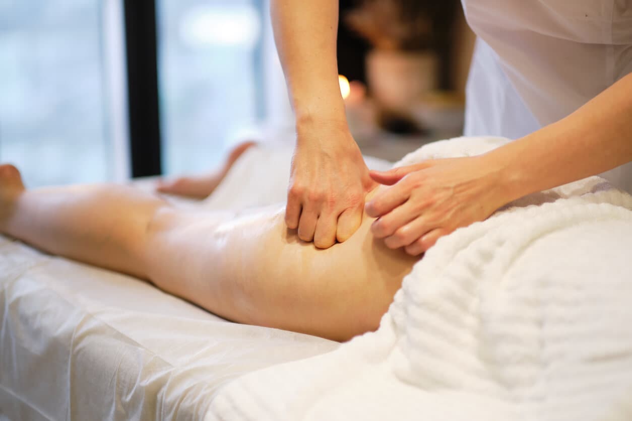 Profissional realizando drenagem linfática manual nas pernas de uma paciente