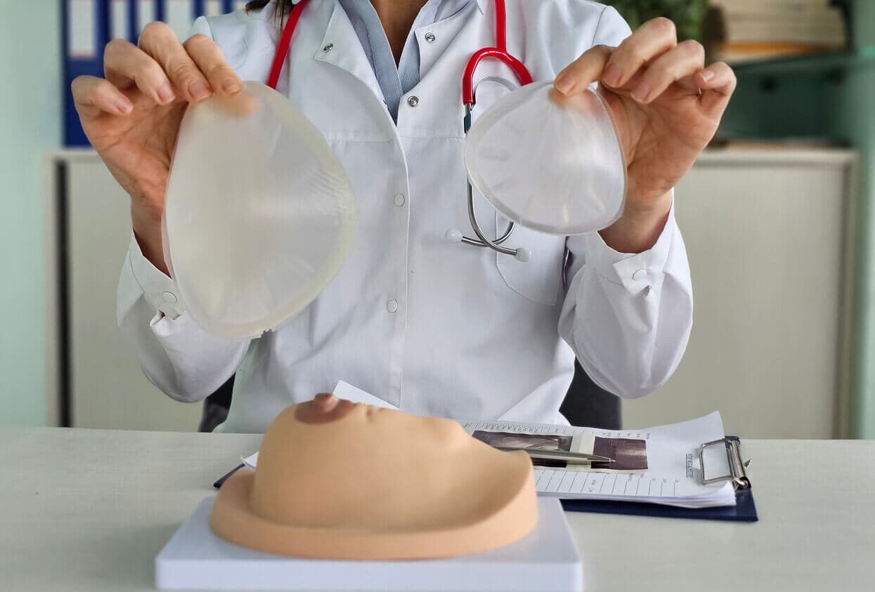 Médica sentada em consultório segurando duas próteses de silicone de tamanho e volumes diferentes