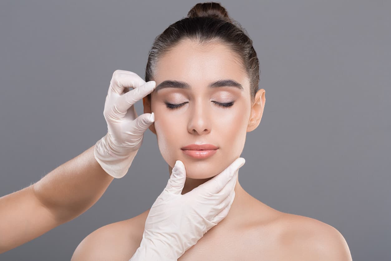 Mãos enluvadas tocando o rosto de uma mulher, indicando as regiões de tratamento do microlifting facial