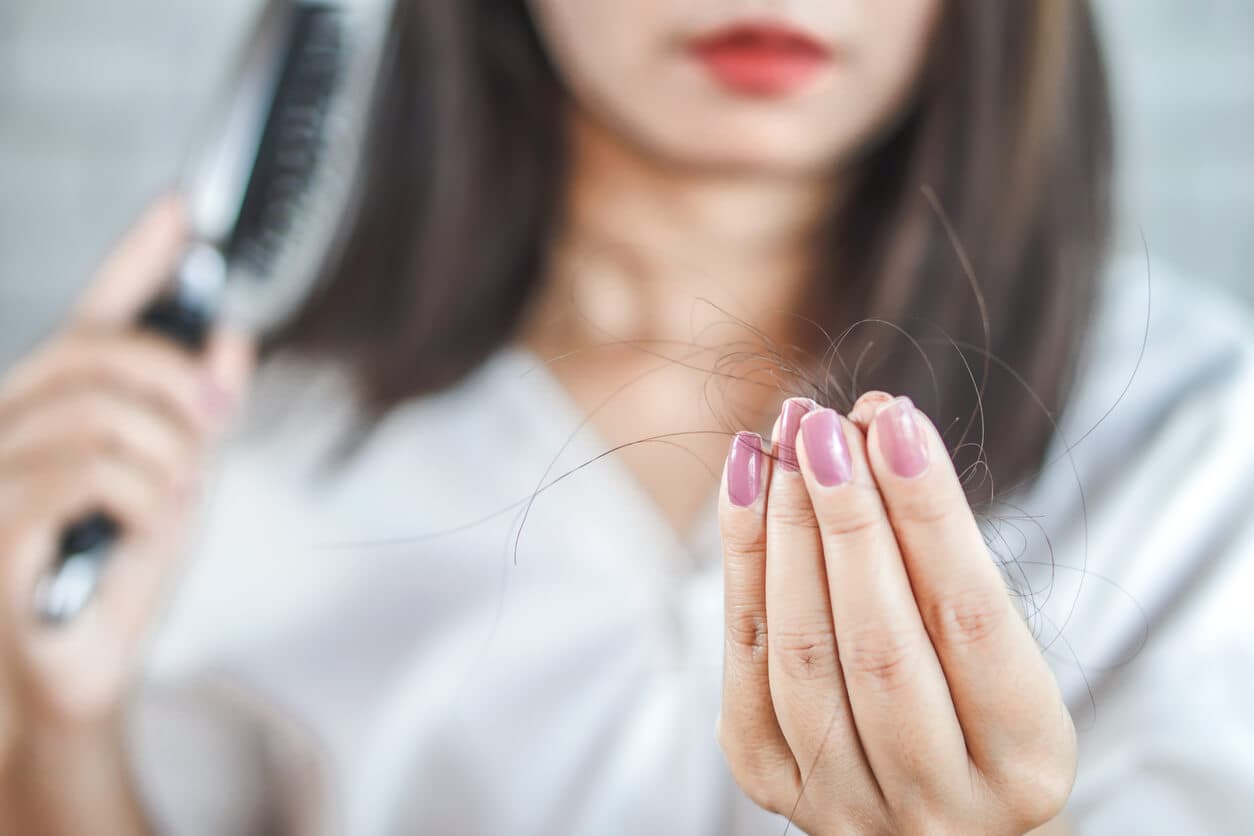 Mulher segurando fios de cabelo nas mãos, observando a queda após pentear, ilustrando preocupação com calvície e tratamentos capilares.