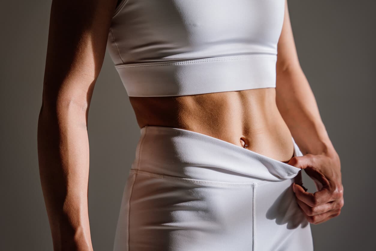 Mulher com roupas esportivas brancas expondo o abdômen firme e definido