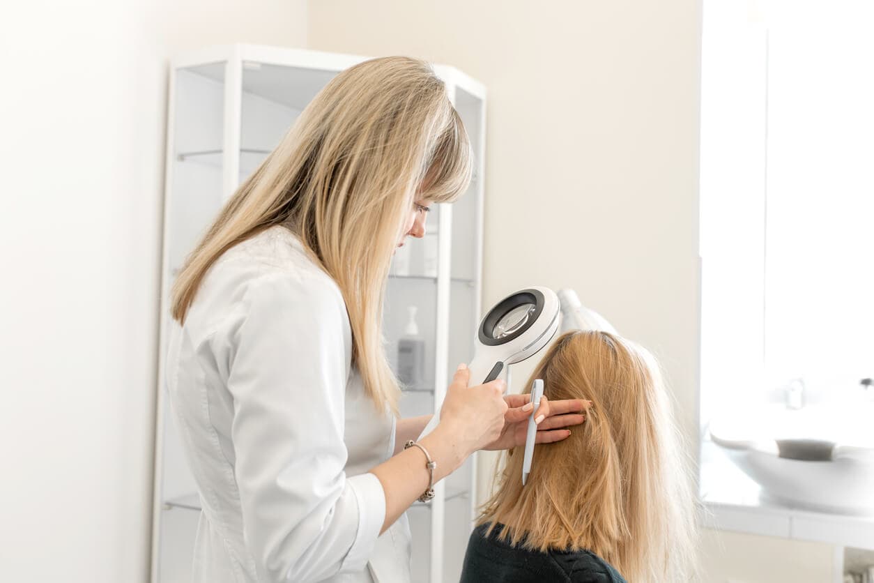 Médica tricologista examinando couro cabeludo de uma paciente durante consulta.