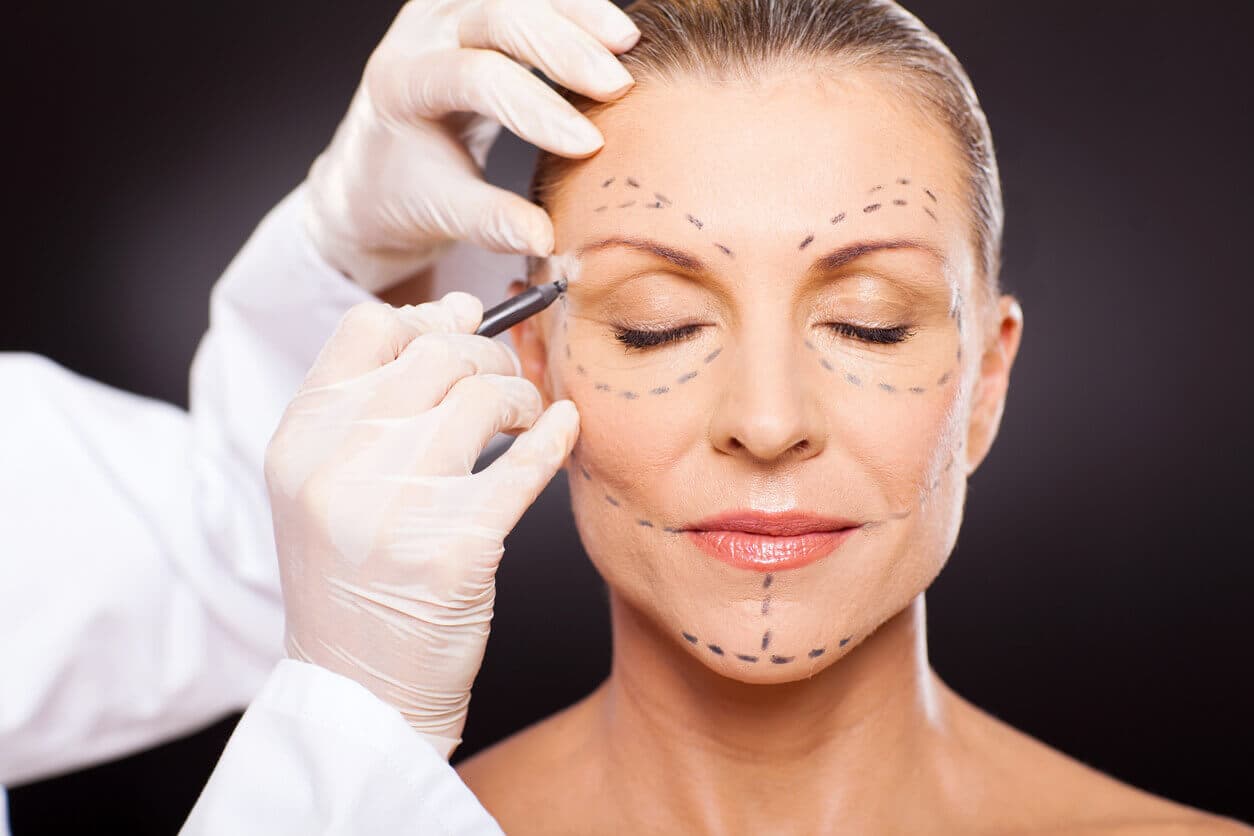 Médica realiza marcações no rosto de uma paciente durante avaliação para procedimento de rejuvenescimento facial.
