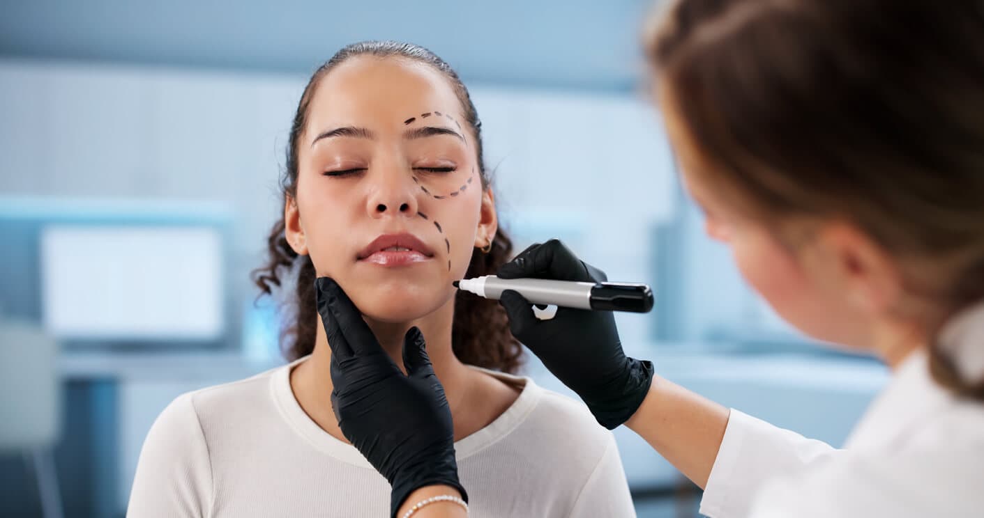 Médica marca áreas do rosto de uma paciente para planejar um lifting facial.