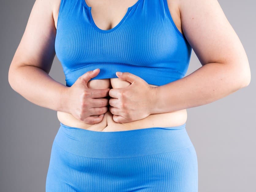 Mulher com roupa esportiva azul segurando a região abdominal com sinais de diástase.