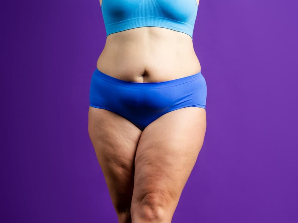 Abdômen e parte superior das pernas de uma mulher usando roupa íntima azul e fundo roxo