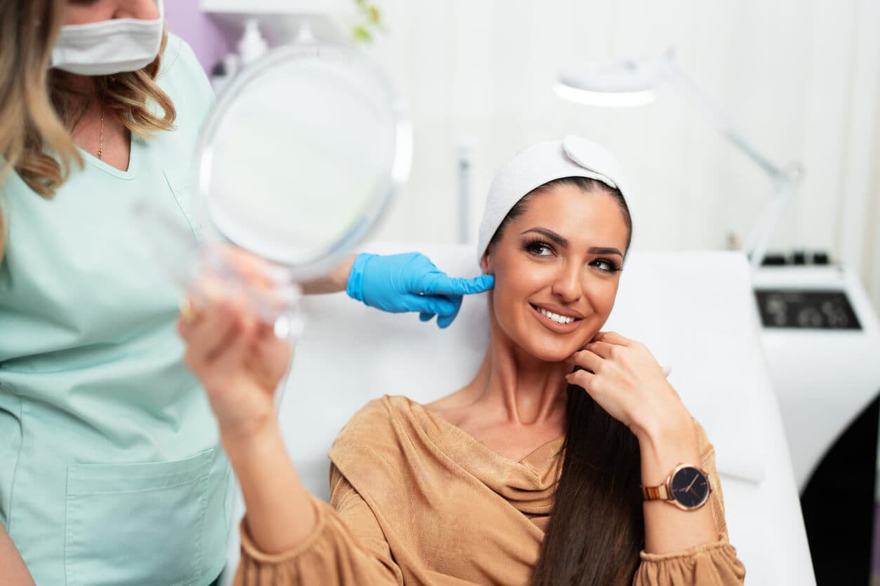 Paciente olhando-se no espelho satisfeita após procedimento com toxina botulínica