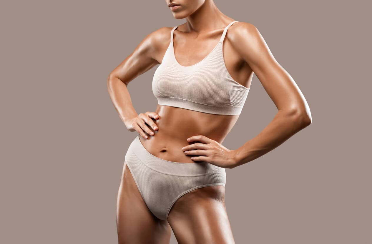 Mulher com corpo definido e postura ereta usa conjunto de roupa íntima bege, representando os resultados estéticos da lipoaspiração e o contorno corporal após o procedimento.