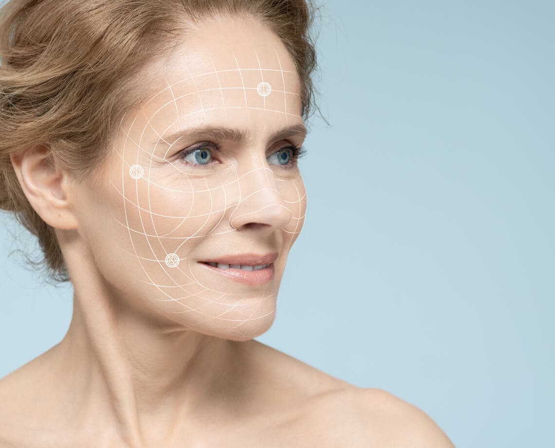 Mulher madura em close de perfil, com marcações gráficas brancas sobre o rosto que sugerem mapeamento facial e rejuvenescimento