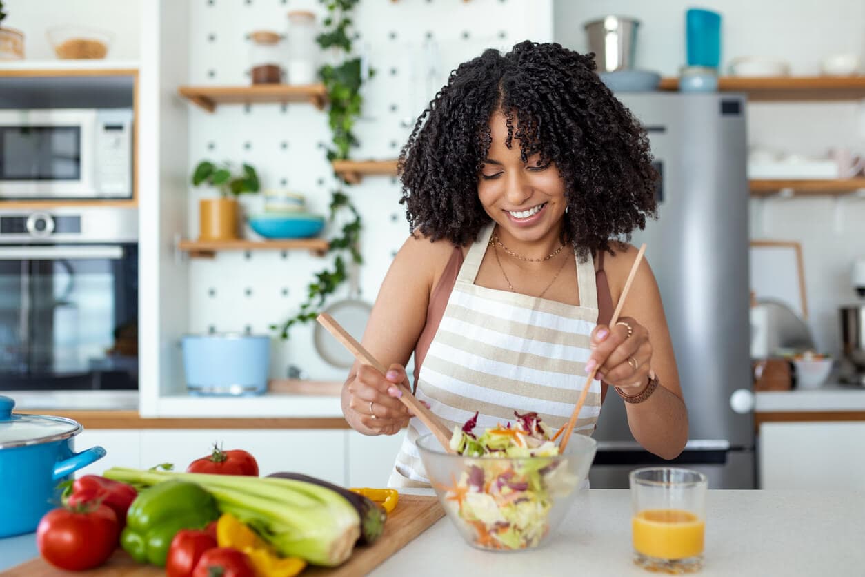 Mulher preparando salada com legumes frescos em cozinha clara