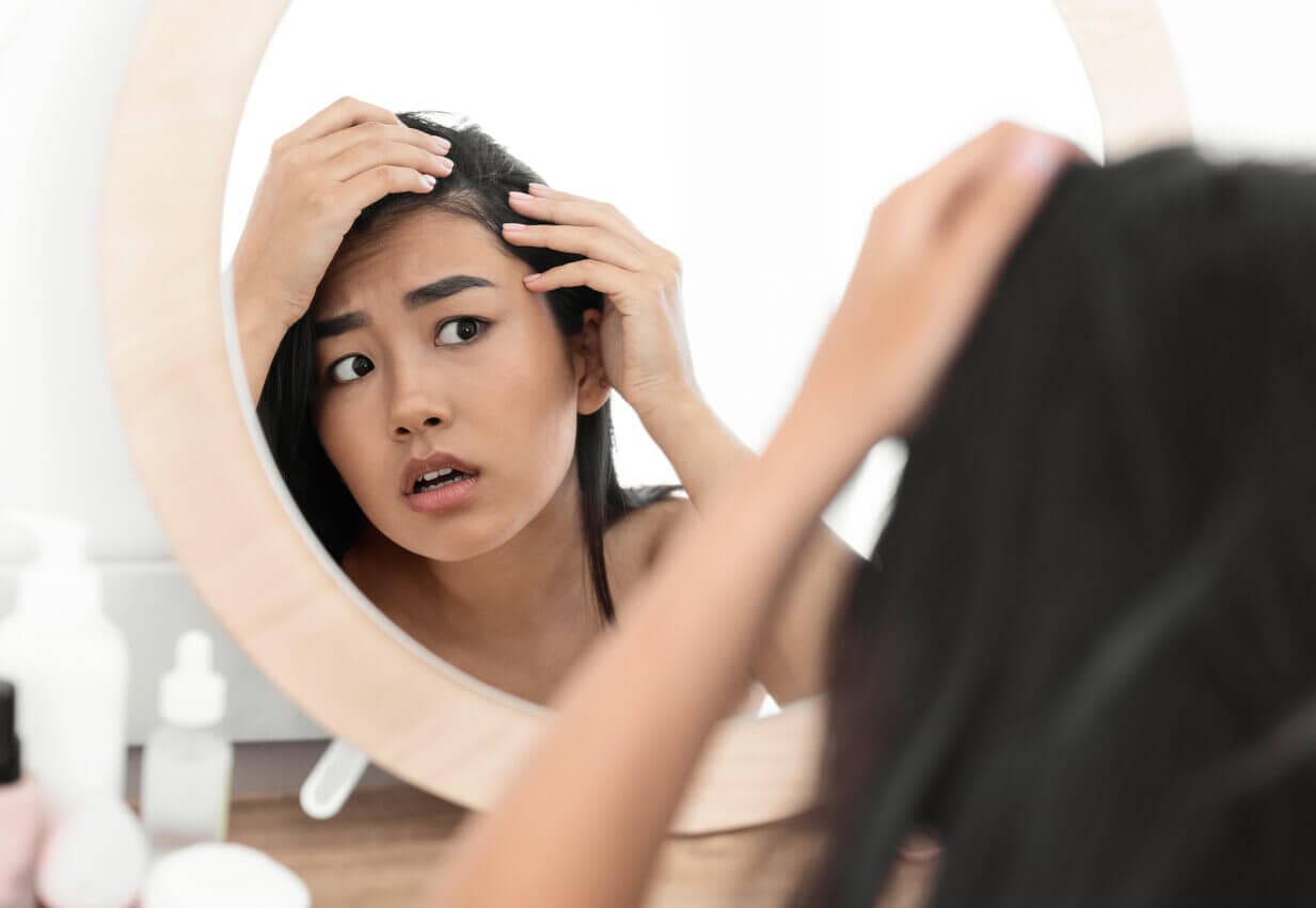 Mulher preocupada observando áreas de queda de cabelo no espelho