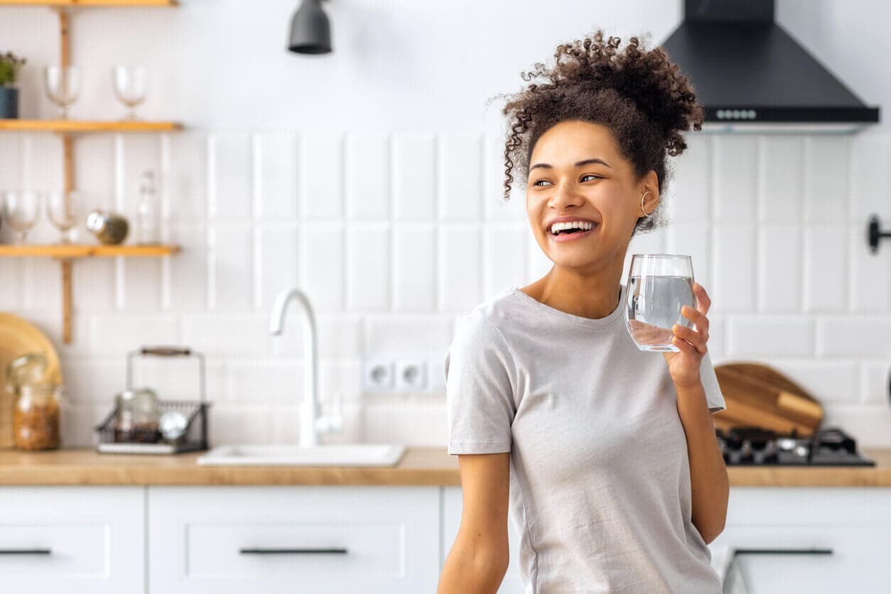 Mulher jovem em uma cozinha com um copo de água na mão
