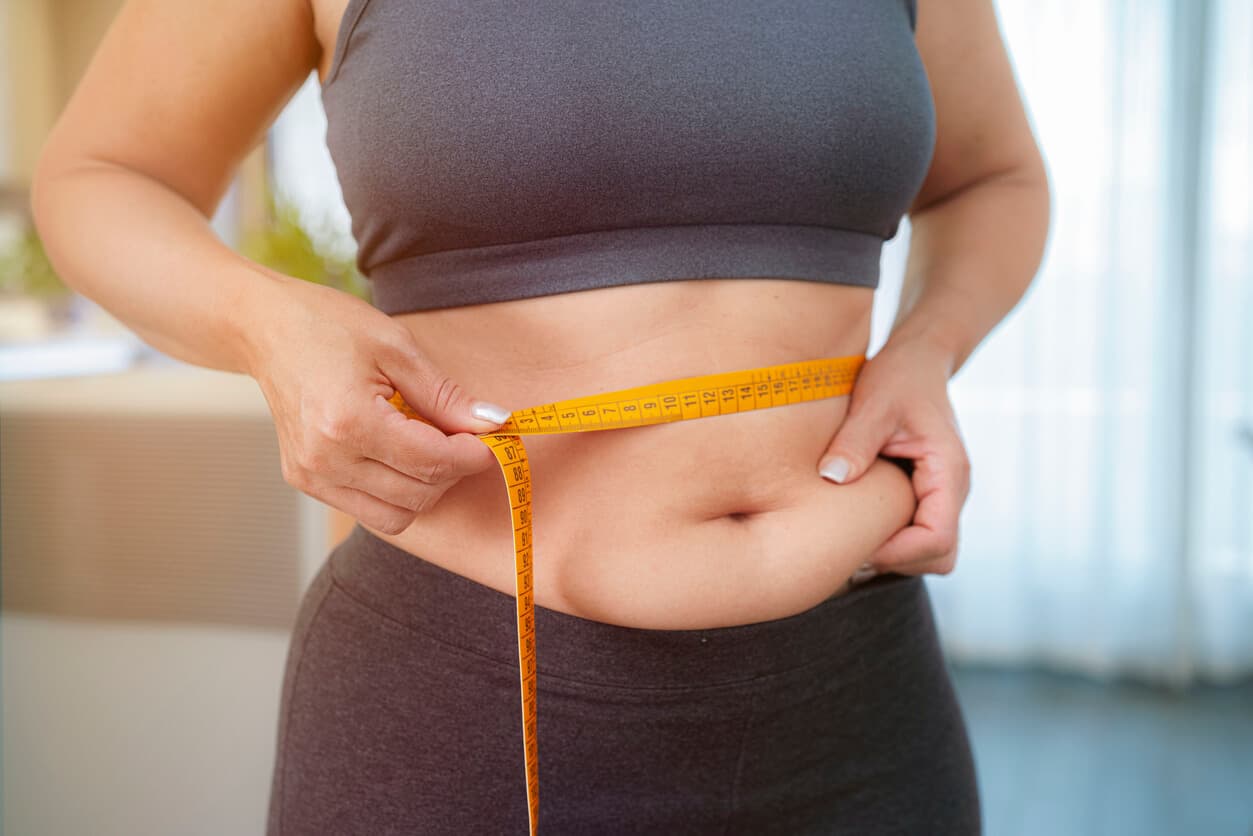 Mulher com gordura abaixo do umbigo mede a região abdominal com fita métrica.