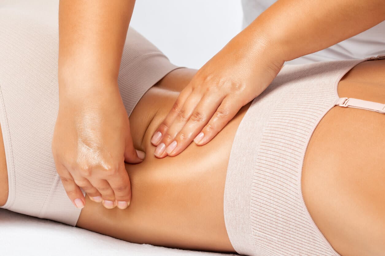 Mulher recebendo massagem modeladora na região abdominal durante sessão de tratamento estético.
