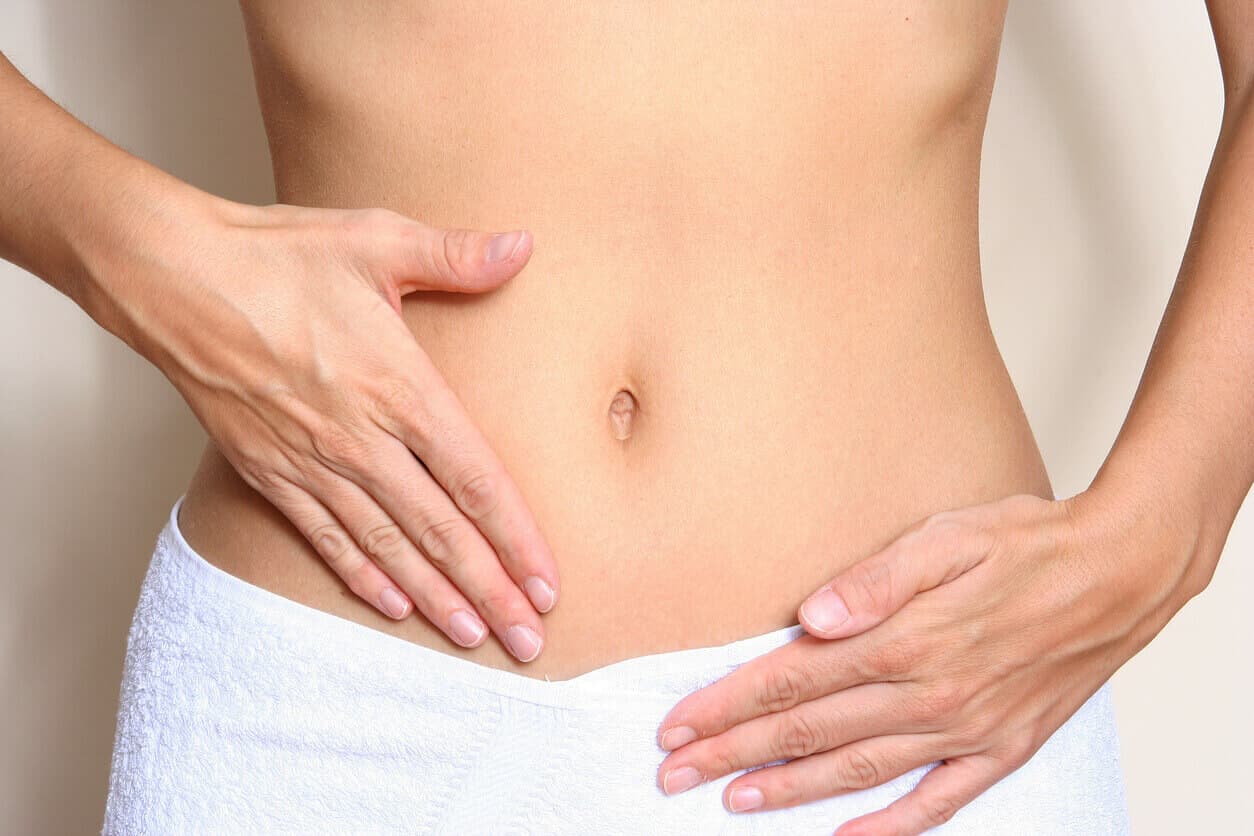 Mulher com as mãos sobre a região pélvica, simbolizando cuidados no pós-operatório de ninfoplastia, com foco na recuperação e alívio do inchaço.