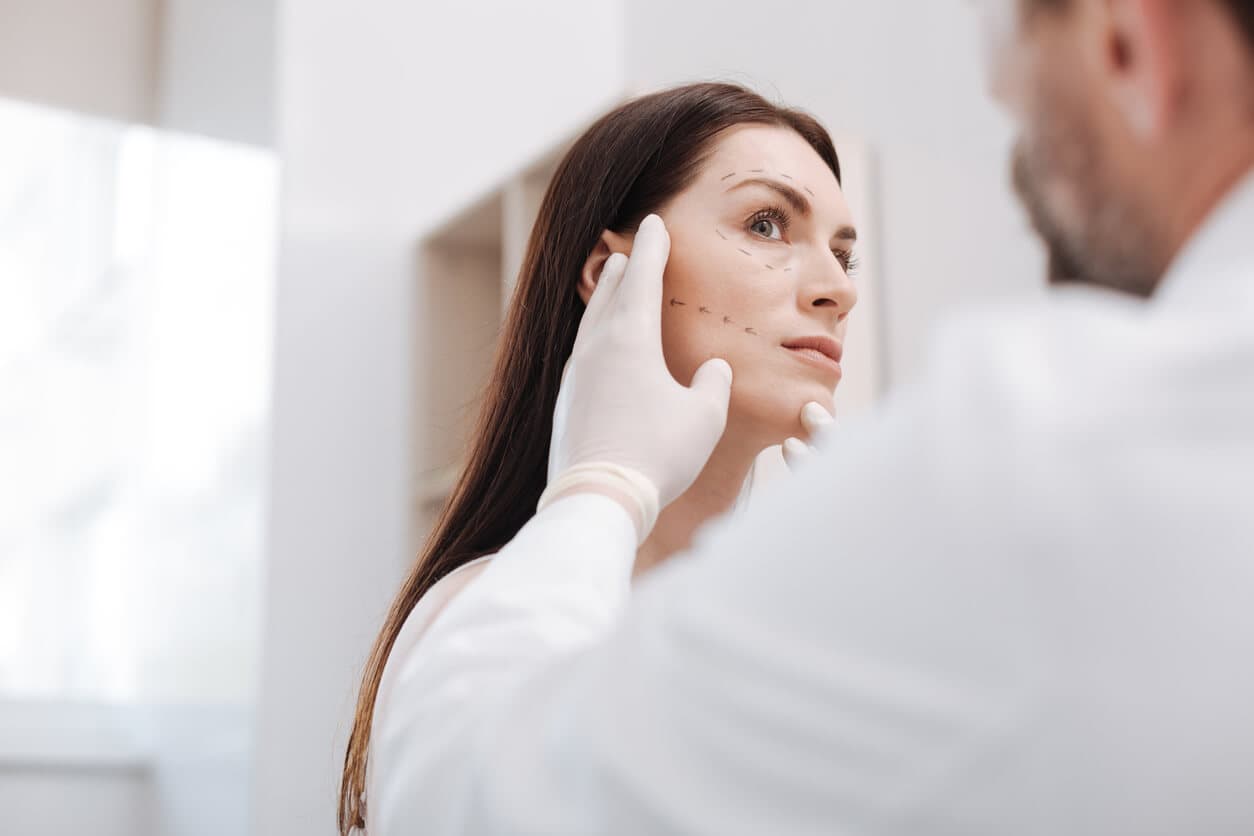 Médico cirurgião realizando preparação no rosto de uma paciente prestes a realizar preenchimento facial