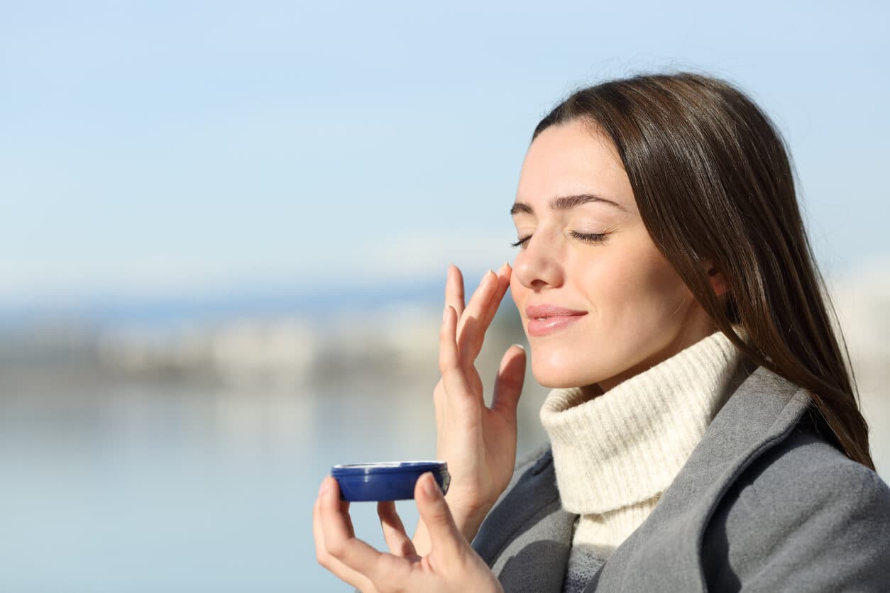 Mulher jovem ao ar livre, em roupas de inverno, aplicando protetor de solar