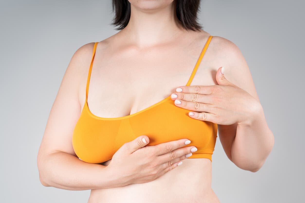 Close de uma mulher com sutiã laranja, levando as mãos aos seios