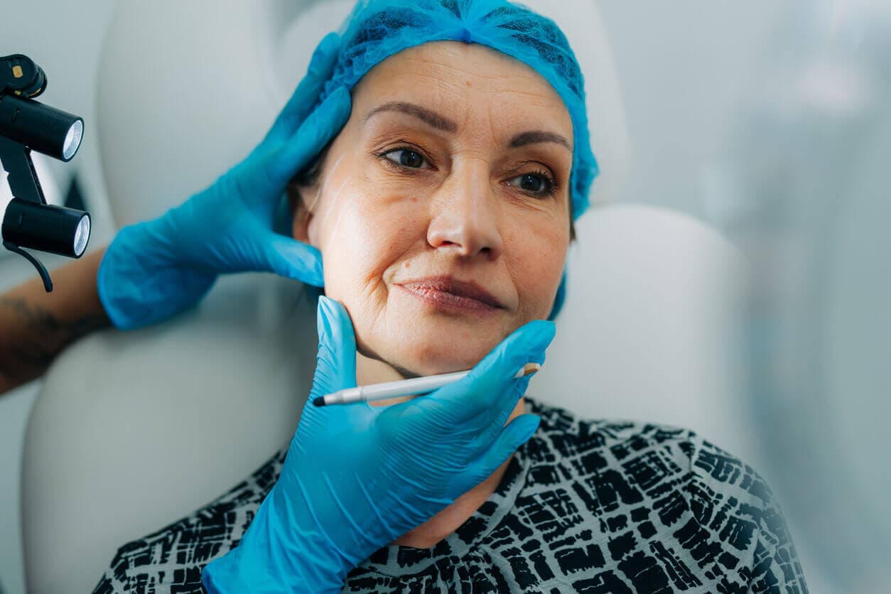 Mulher madura em consulta estética, com profissional avaliando e marcando a região do rosto e do queixo.