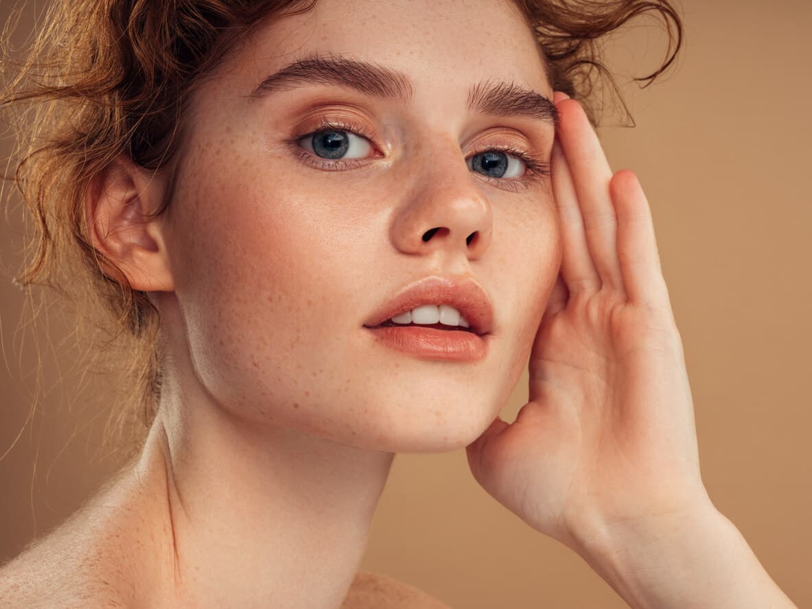 Mulher jovem e ruiva, com a mão apoiada no rosto