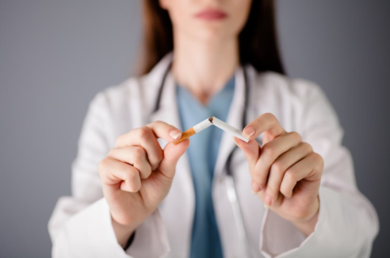 Médica quebrando um cigarro ao meio, evidenciando a importância de parar de fumar