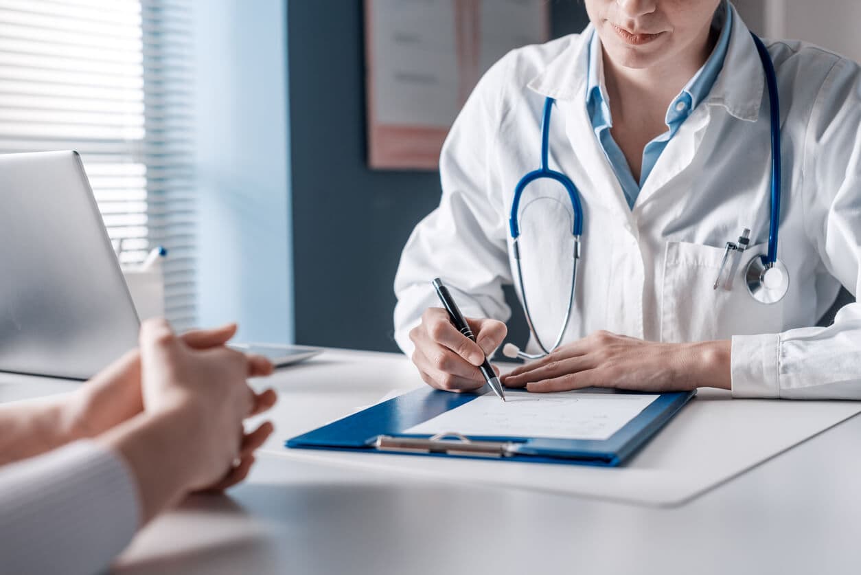 Médico escrevendo em prancheta durante consulta com paciente