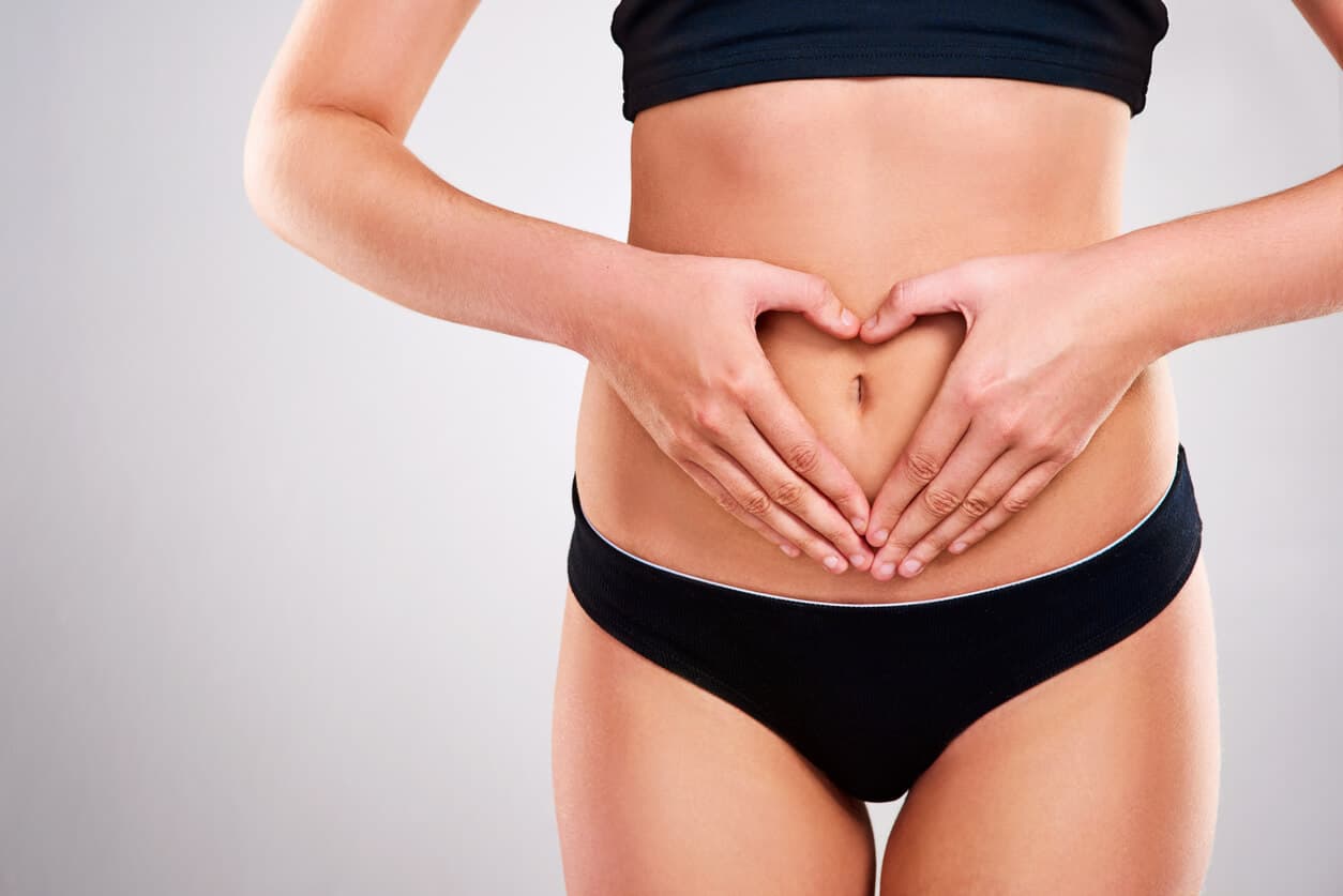 Mulher com as mãos formando um coração sobre o umbigo após cirurgia de abdominoplastia