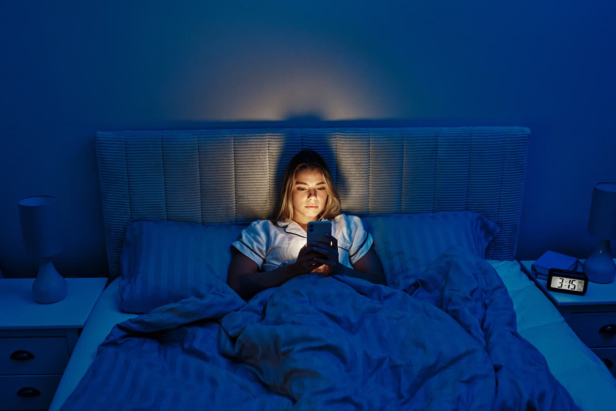 Jovem usando o celular na cama, com as luzes apagadas