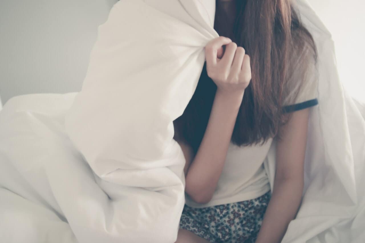 Mulher sentada na cama com cobertor cobrindo seu rosto