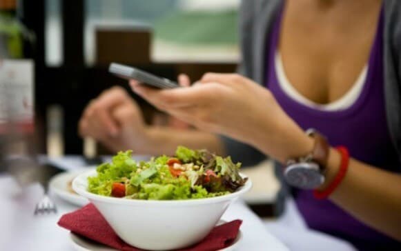 Mulher com celular na mão durante uma refeição da dieta